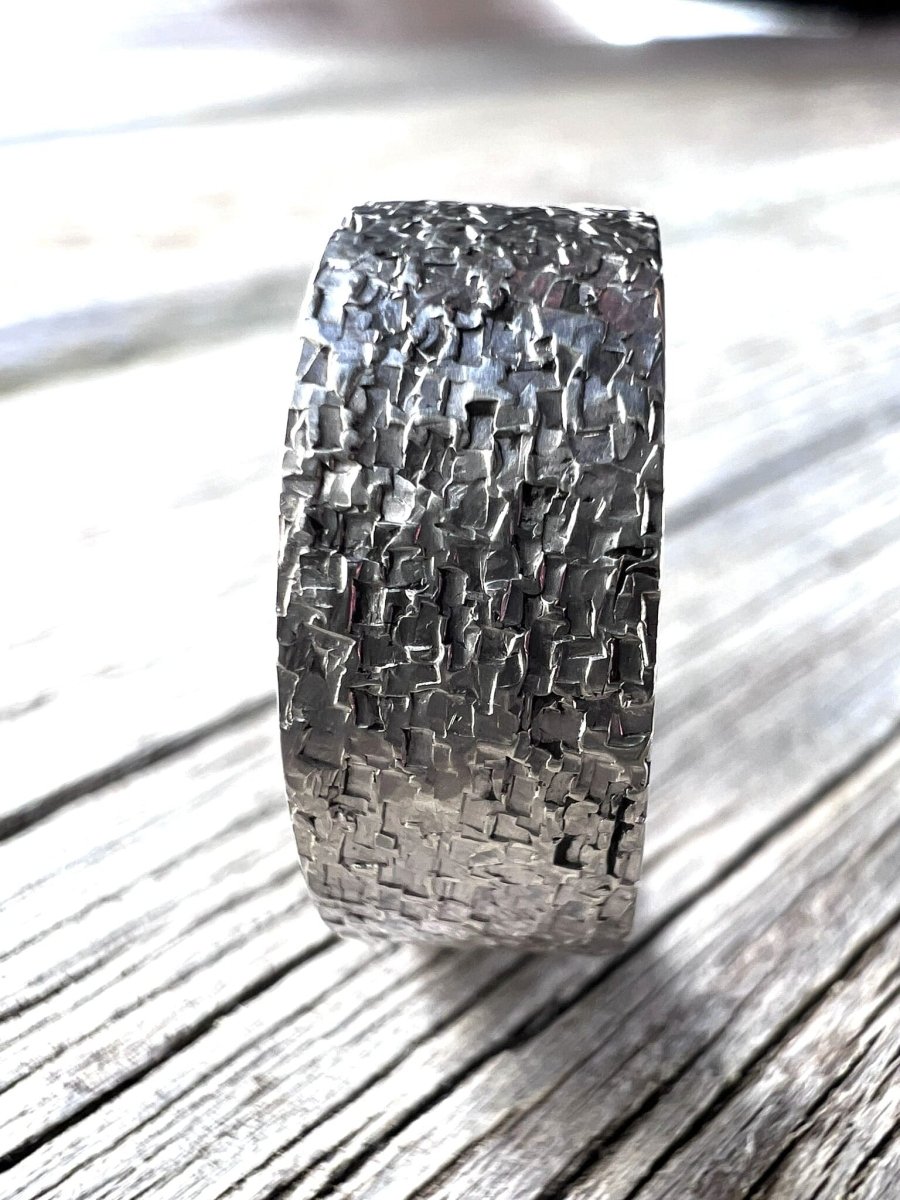 Close-up of a handmade sterling silver wide band ring showing the chipped, irregular surface texture on a plain background