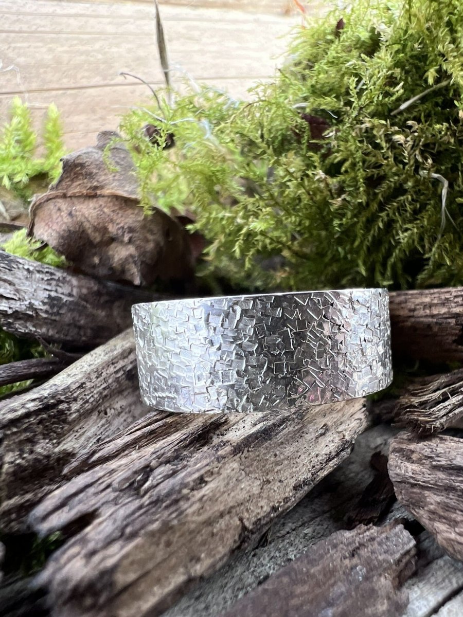 Recycled sterling silver wide band ring with chipped texture resting on weathered wood chips with green moss, handmade jewellery