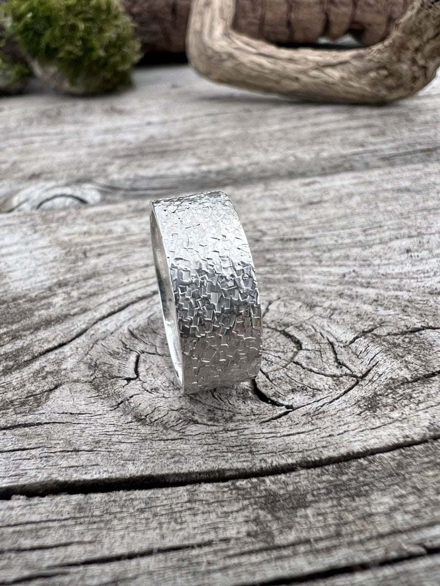 Recycled sterling silver wide band chipped texture ring standing upright on weathered wood with moss in the background