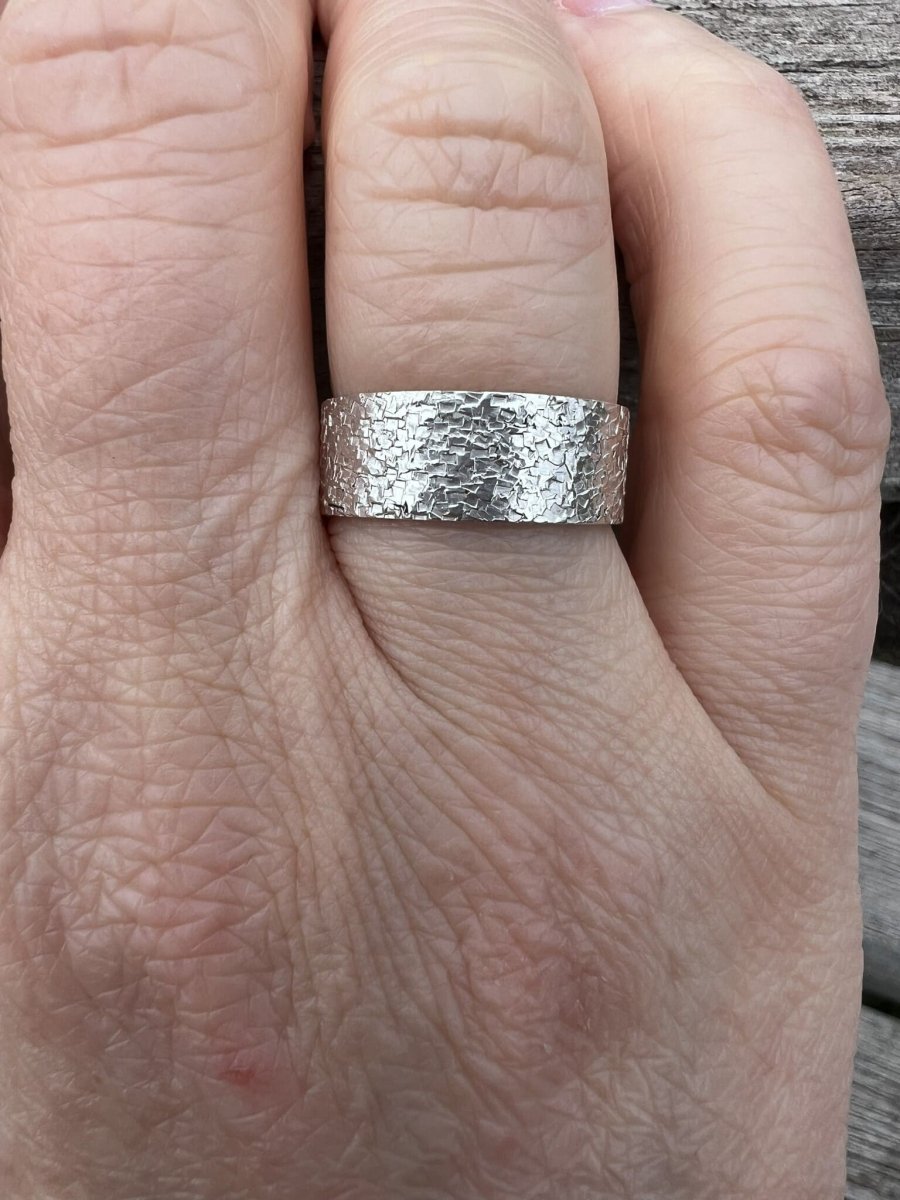 Sterling silver wide band ring with chipped texture worn on a finger, showing scale and the bold statement band